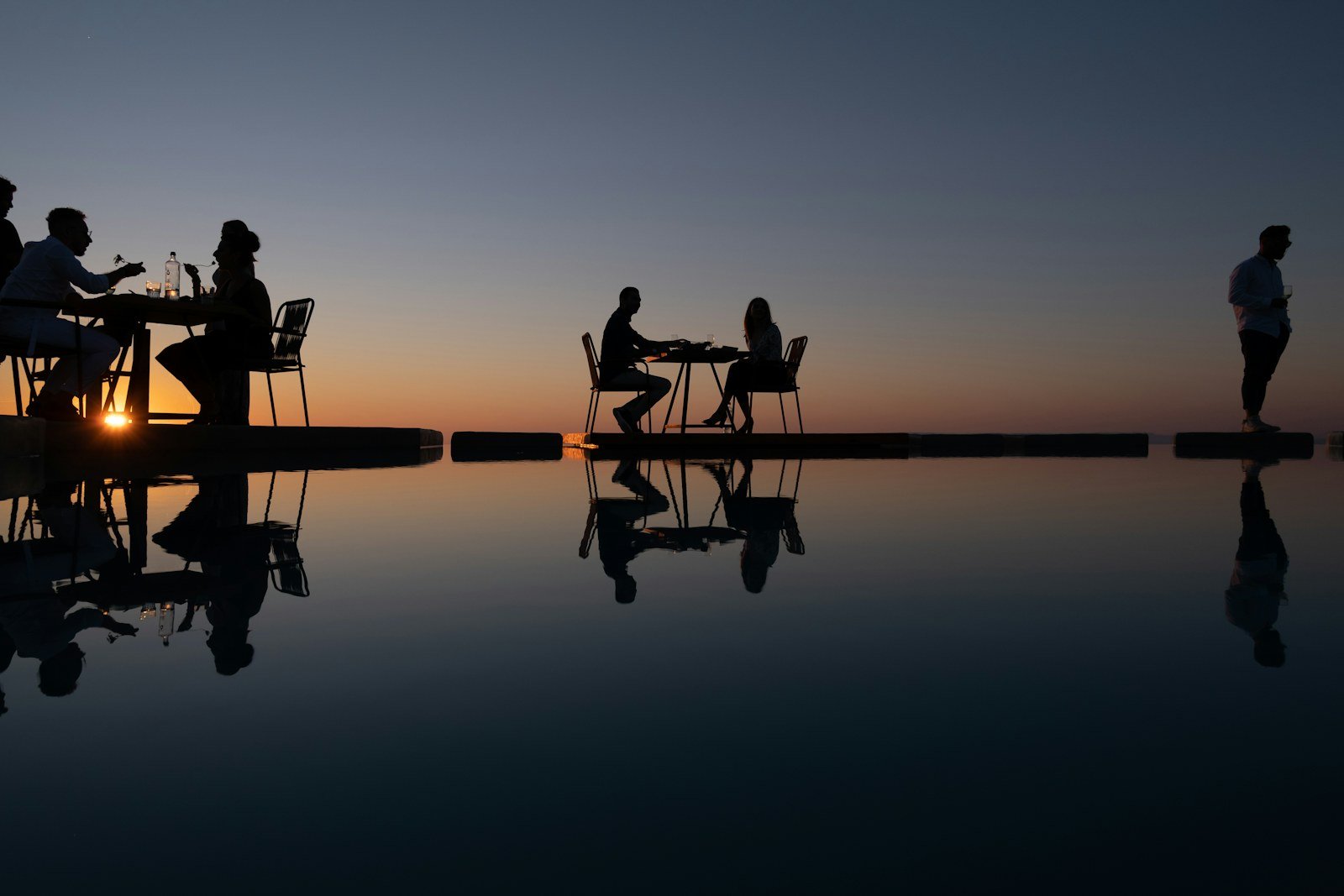 Two figures at a private dining table overlooking the ocean at sunset