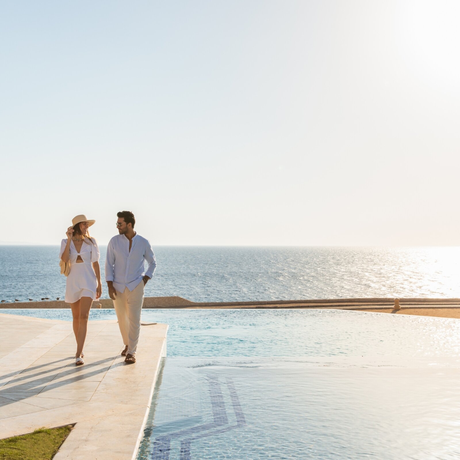 Couple walking by an infinity-pool overlooking the sea