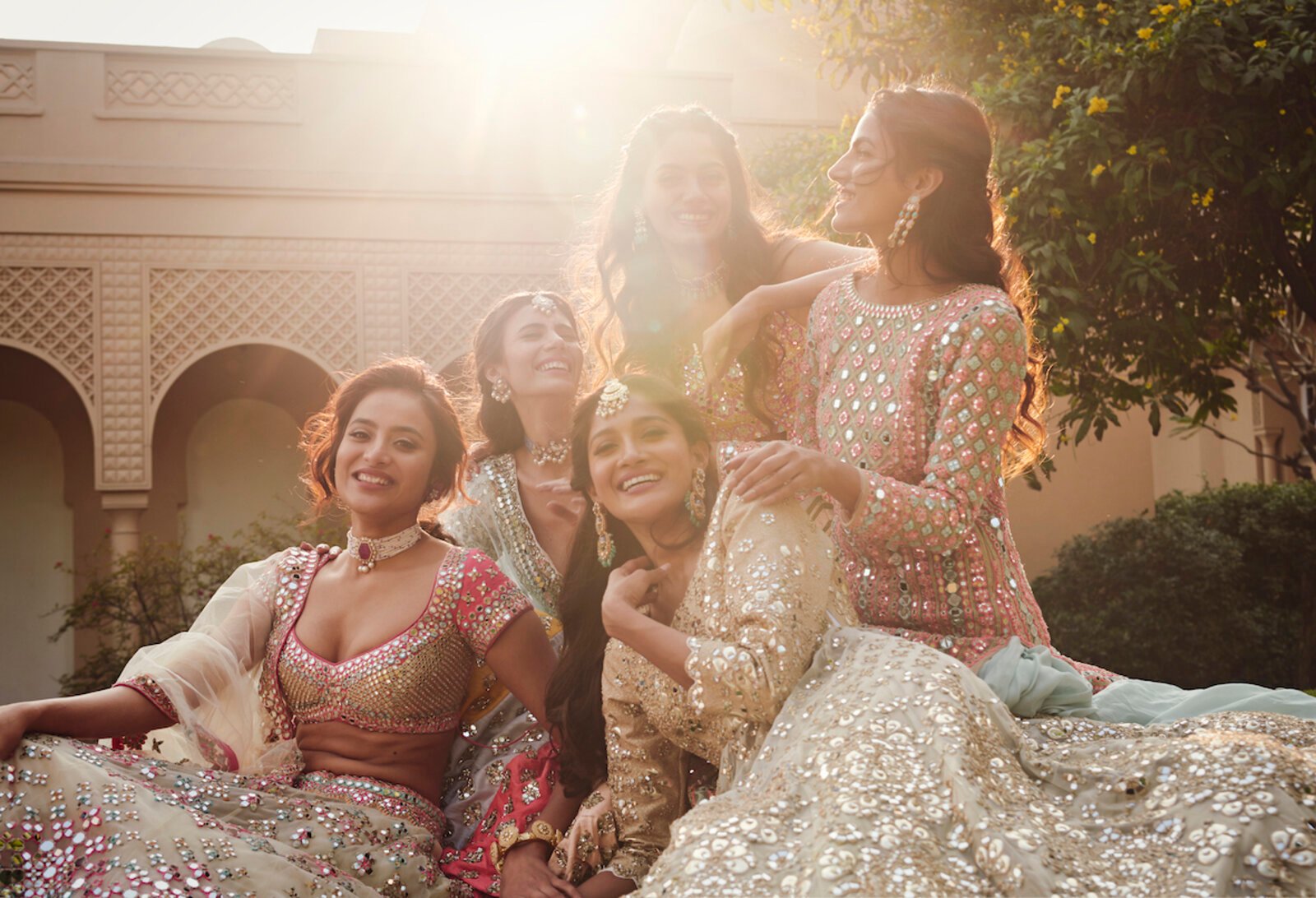 Bride and bridesmaids laughing under arched palace colonnade at golden hour