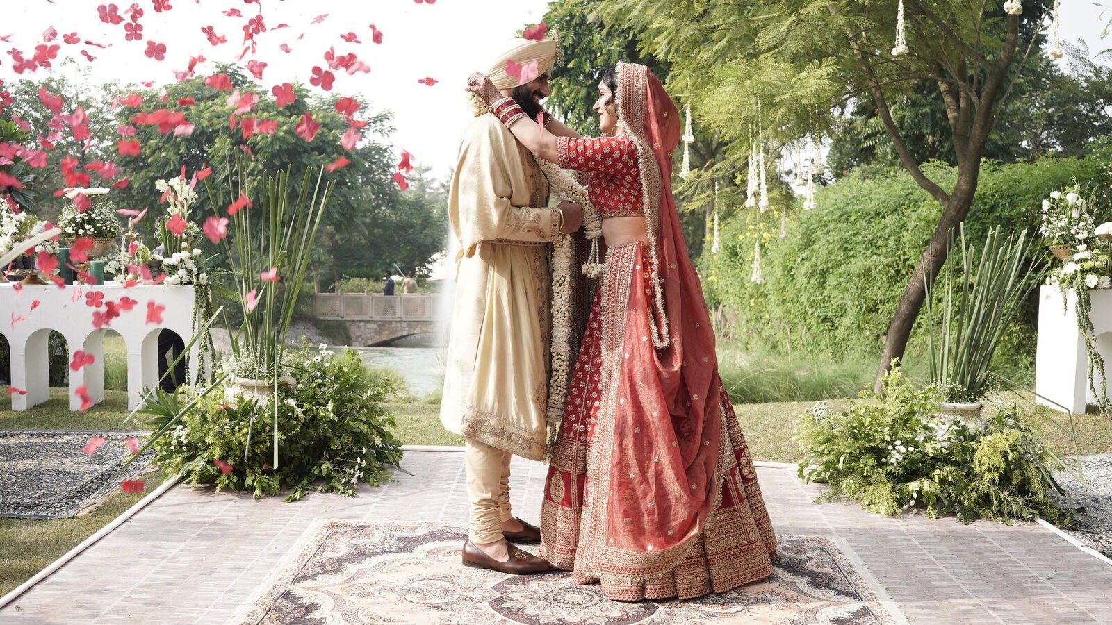 A bride and groom in traditional attire beneath a shower of rose petals at a luxury Indian wedding